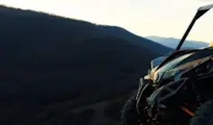 An off-road vehicle is parked on a mountain trail at sunset.